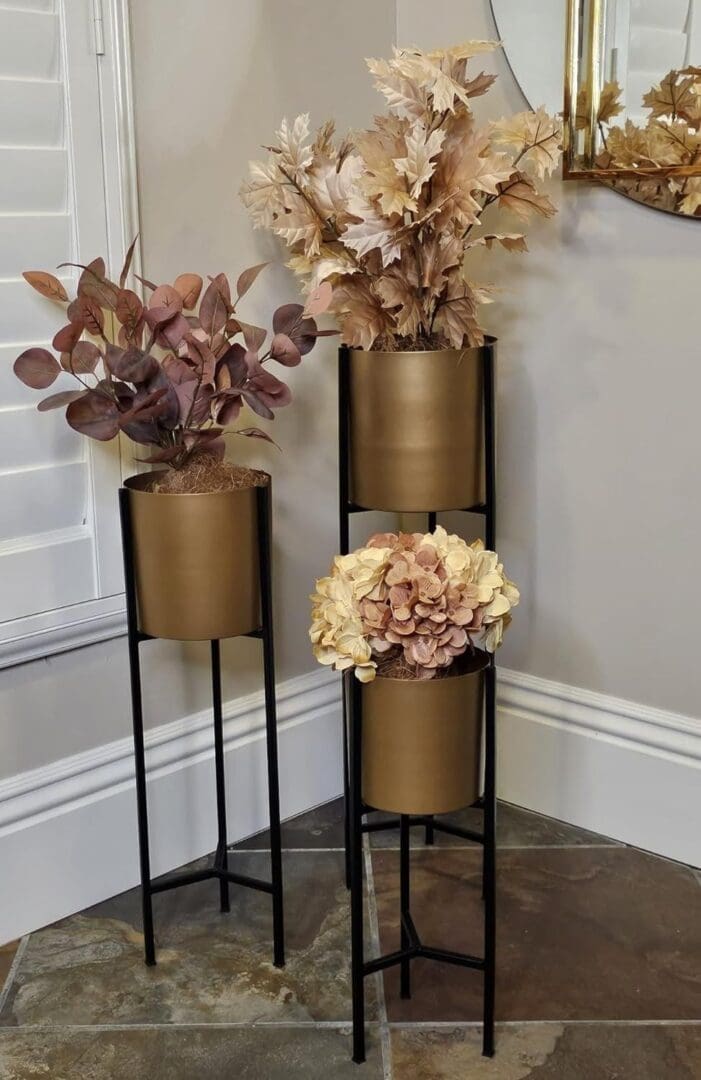 Three gold planters with flowers in them on a floor.