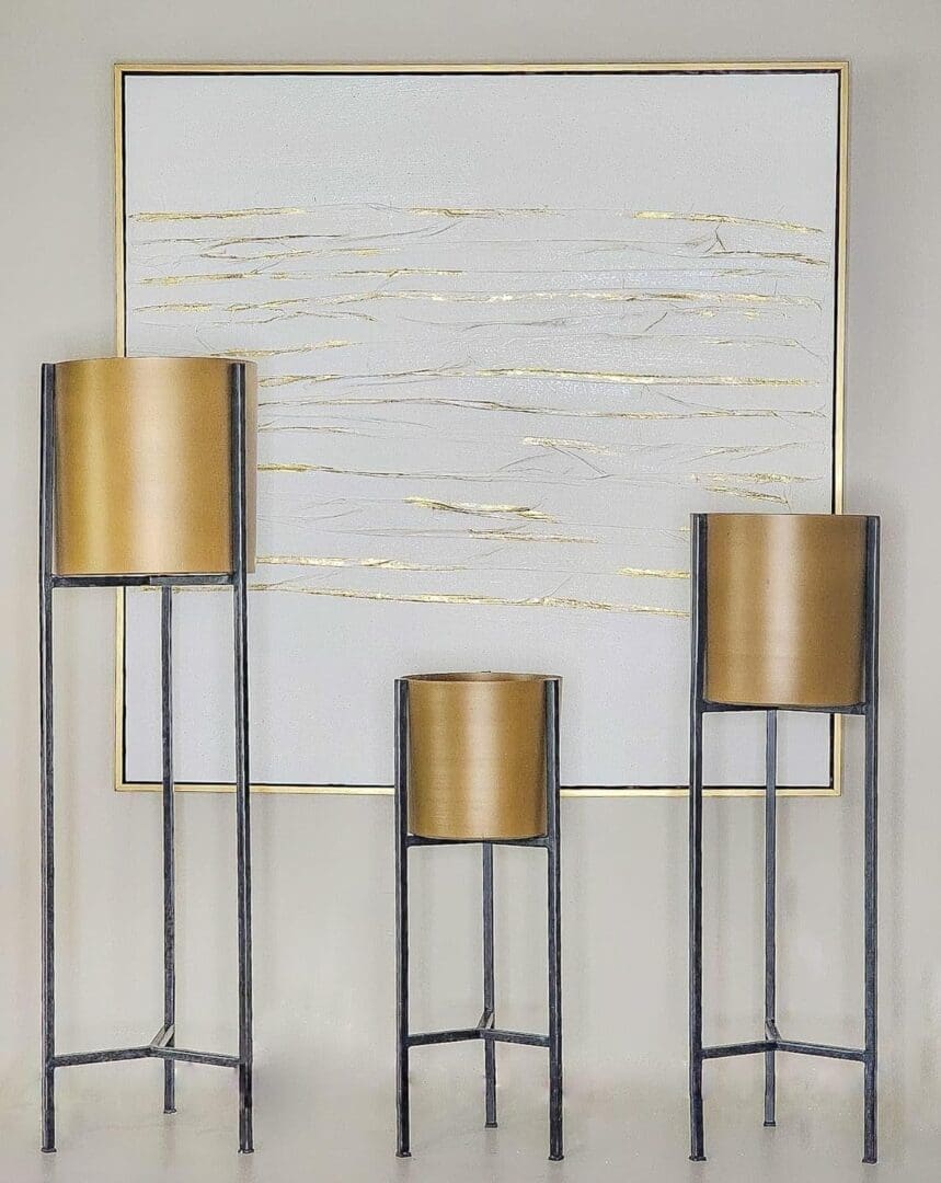 Three tall metal planters with gold colored tops.