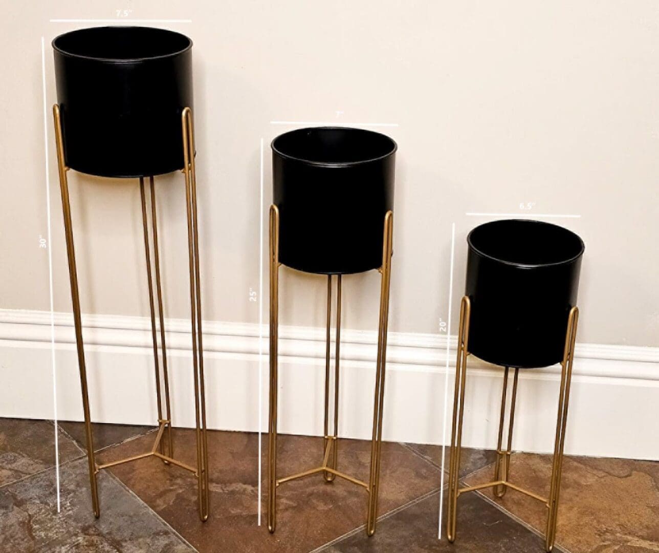 Three black and gold plant stands on a floor.