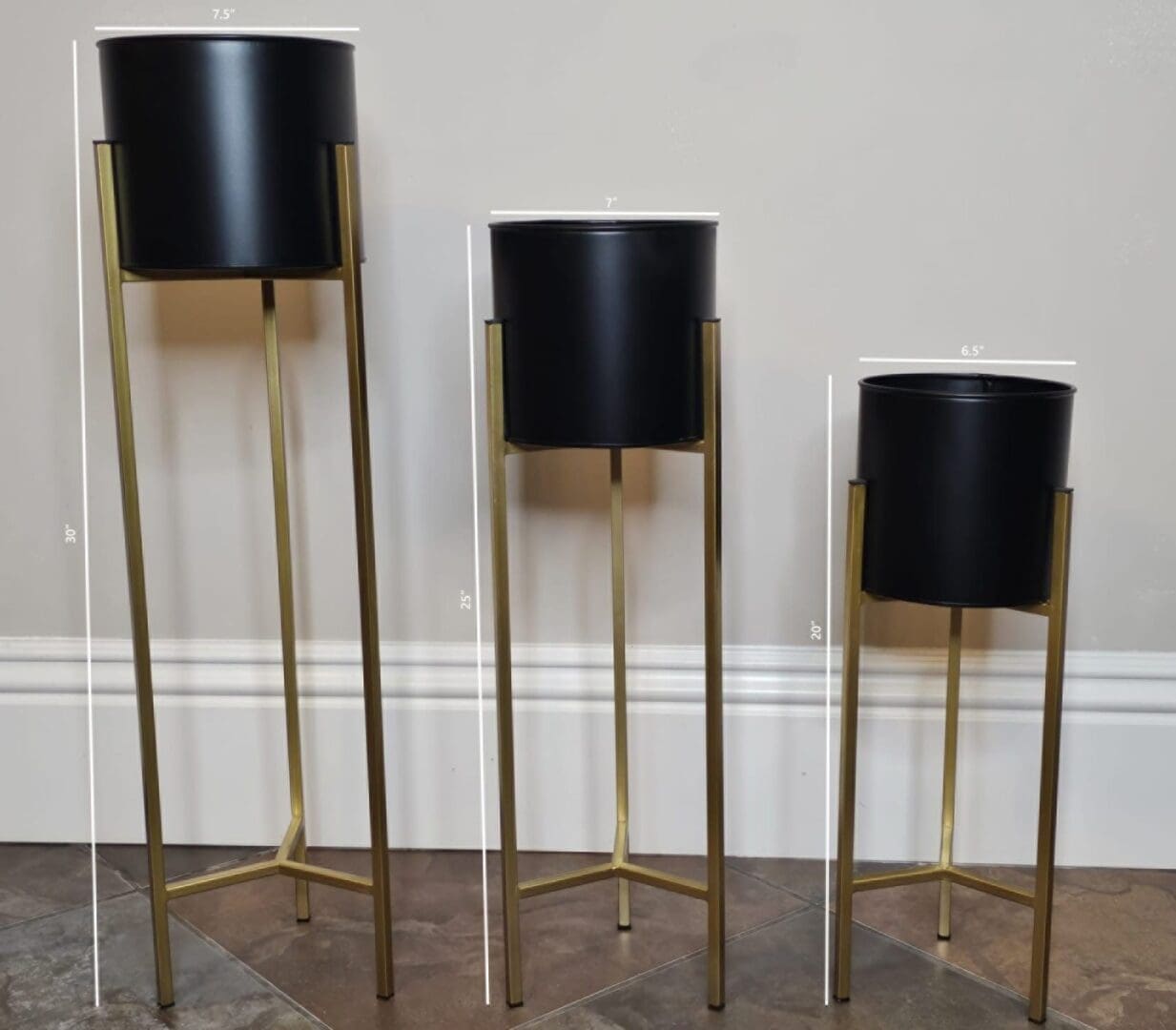 Three tall black planters on stands in a room.