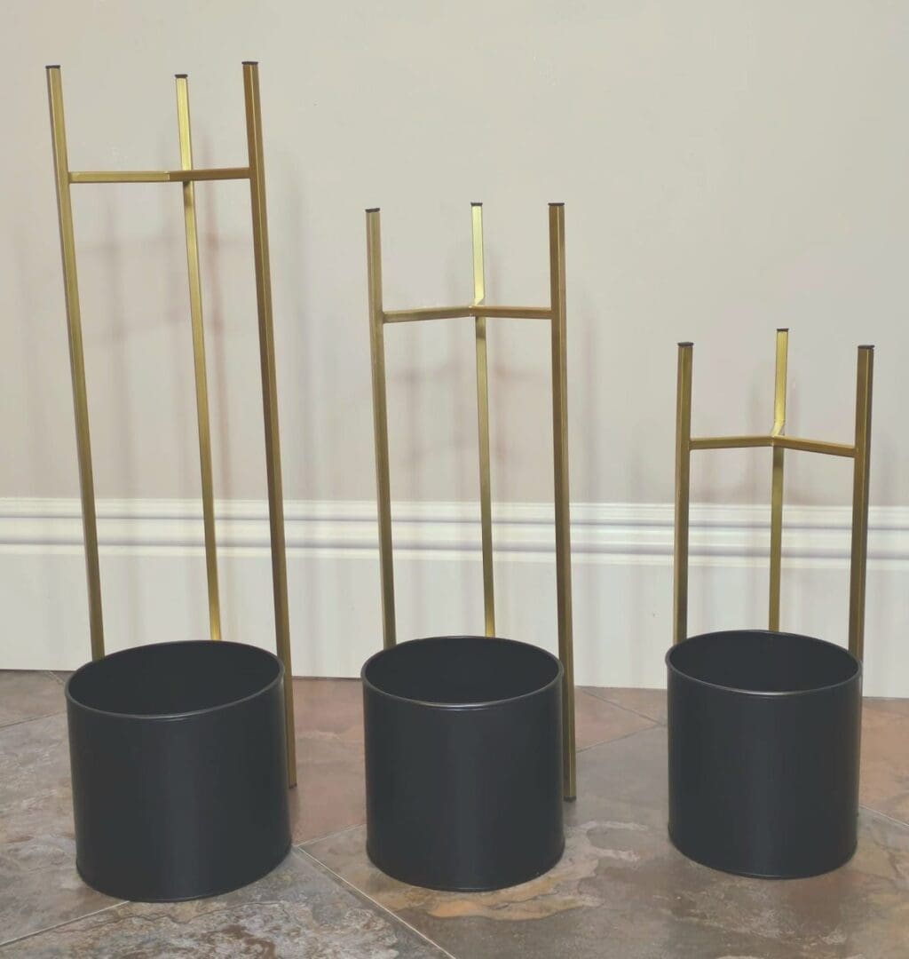 Three black and gold planters are lined up on the floor.