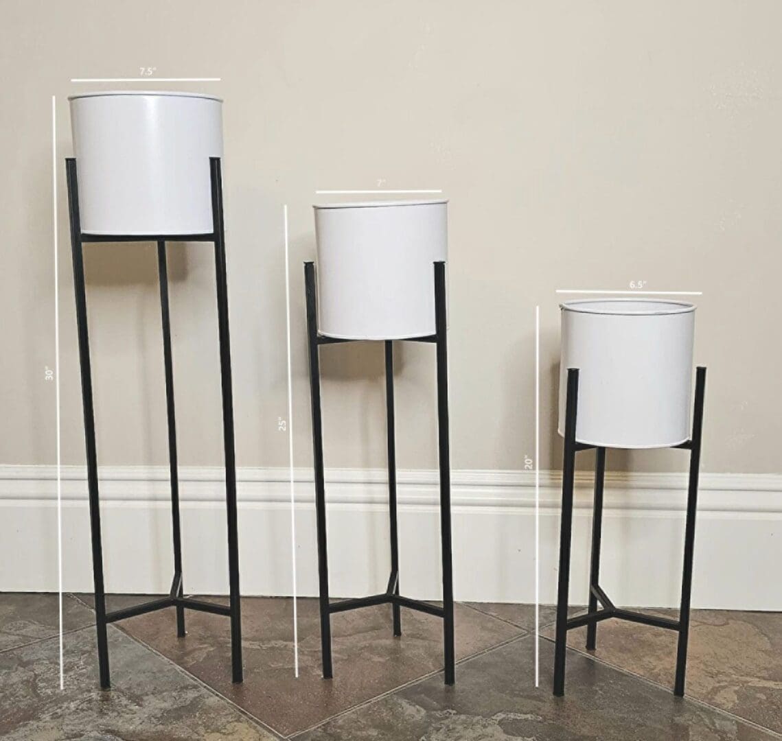 Three tall white pots with stands on a floor.